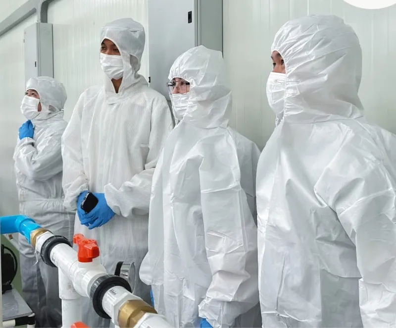 Team in white cleanroom suits inspecting piping in the facility